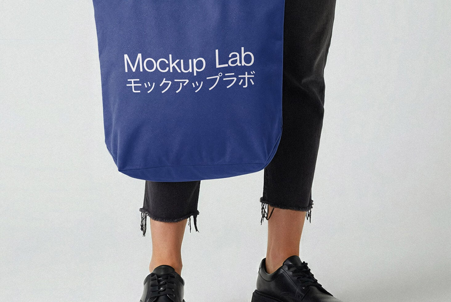 Navy tote bag mockup held by person in ripped black jeans with white typography
