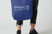 Navy tote bag mockup held by person in ripped black jeans with white typography