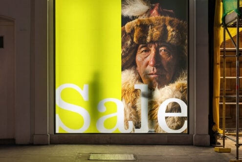 Storefront window at dusk with sale text overlaid on historical portrait of bearded man