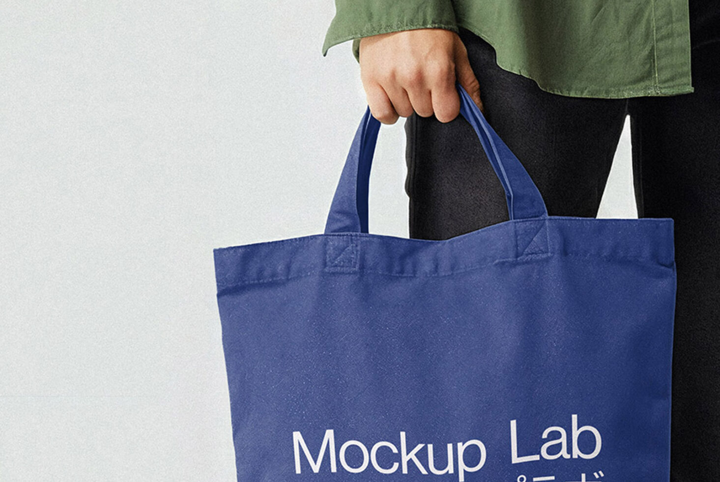 Close up of navy tote bag showing Mockup Lab branding on person wearing green shirt