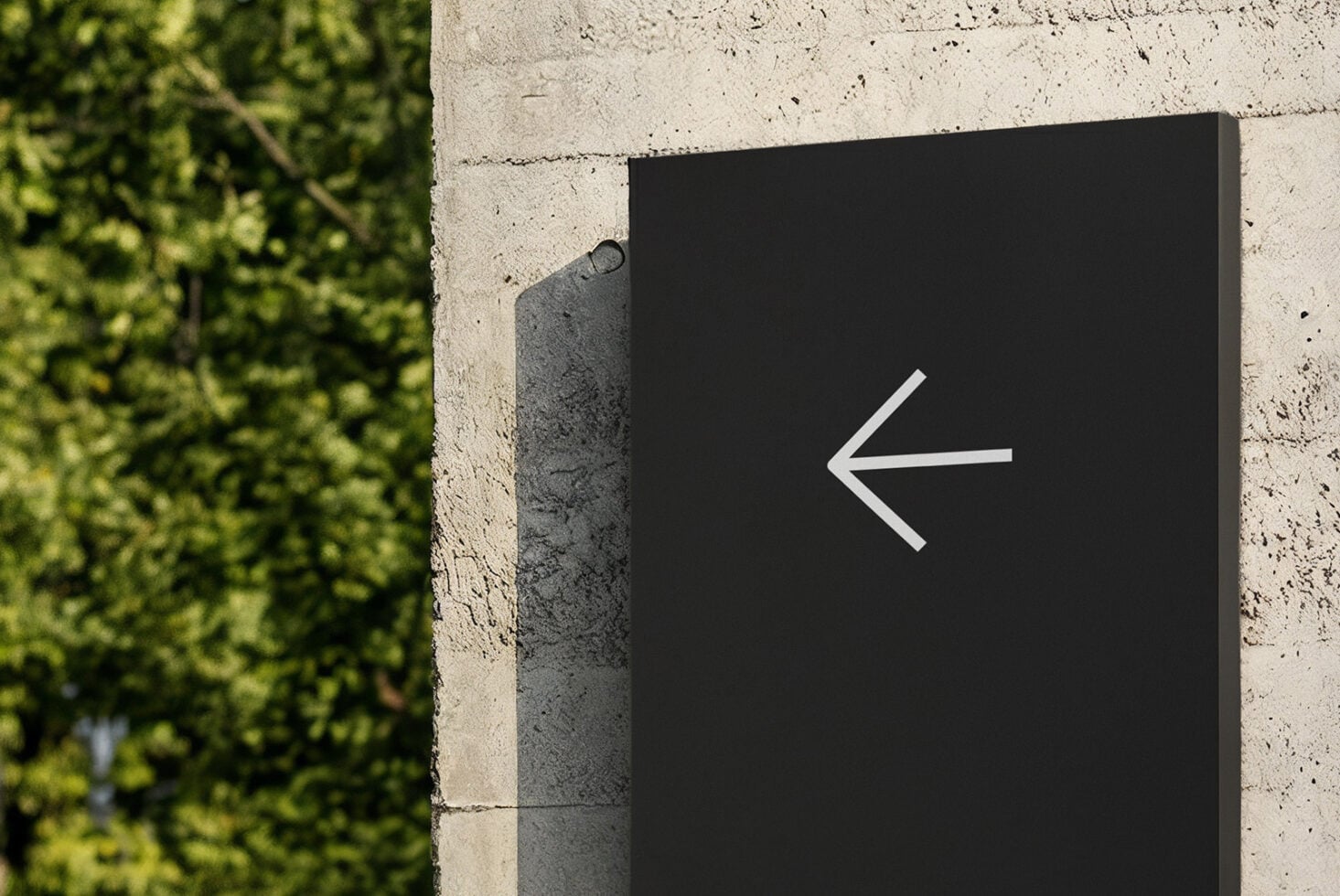 Black wayfinding sign with left arrow on concrete wall