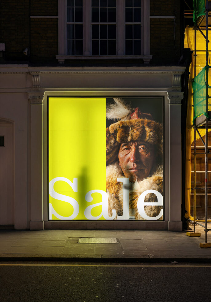 Storefront window at night displaying sale text with bearded man portrait on yellow field