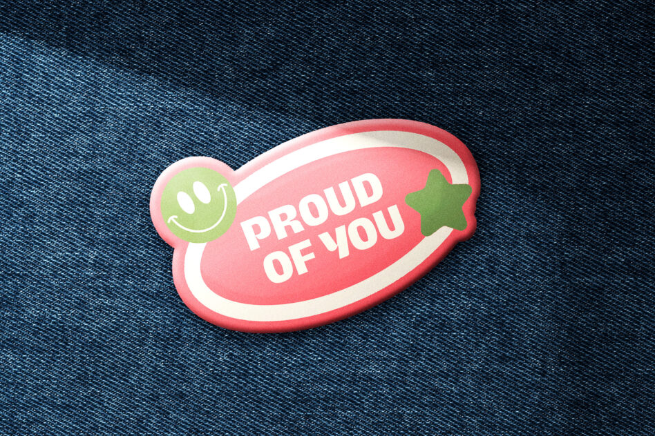 Pink oval badge with smiley face, white text reading Proud Of You on denim
