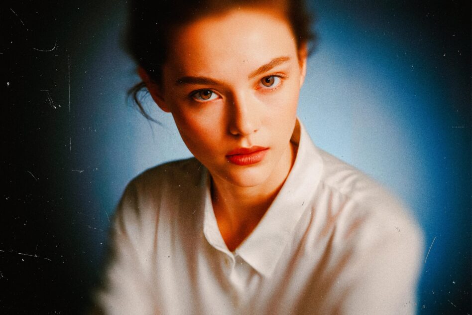 Woman with red hair in white shirt staring directly at camera with blue gradient background
