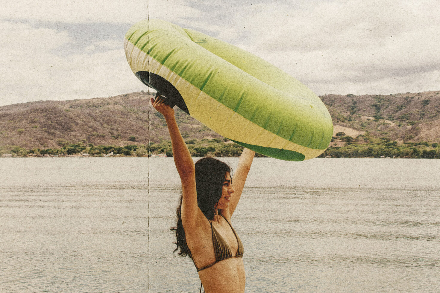 Woman holding inflatable green paraglider above head by water body