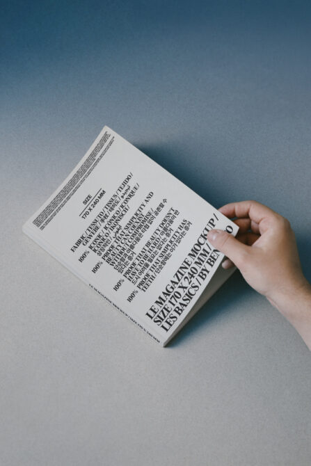 Hand holding white book with multilingual text on blue paper background