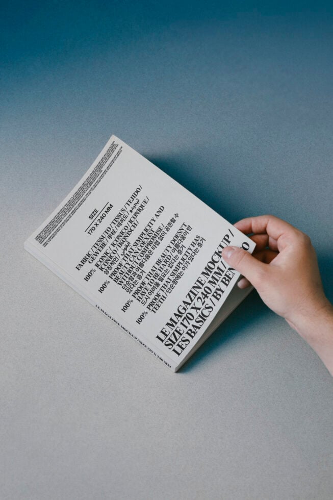 Hand holding white book with multilingual text on blue paper background