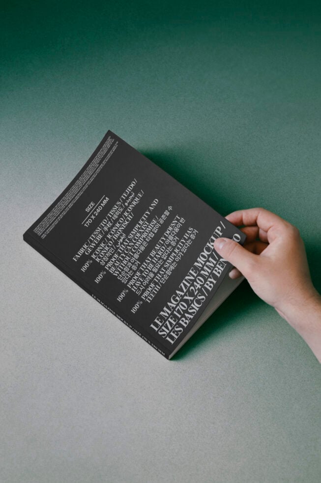 Hand holding dark book with multilingual text on green paper background