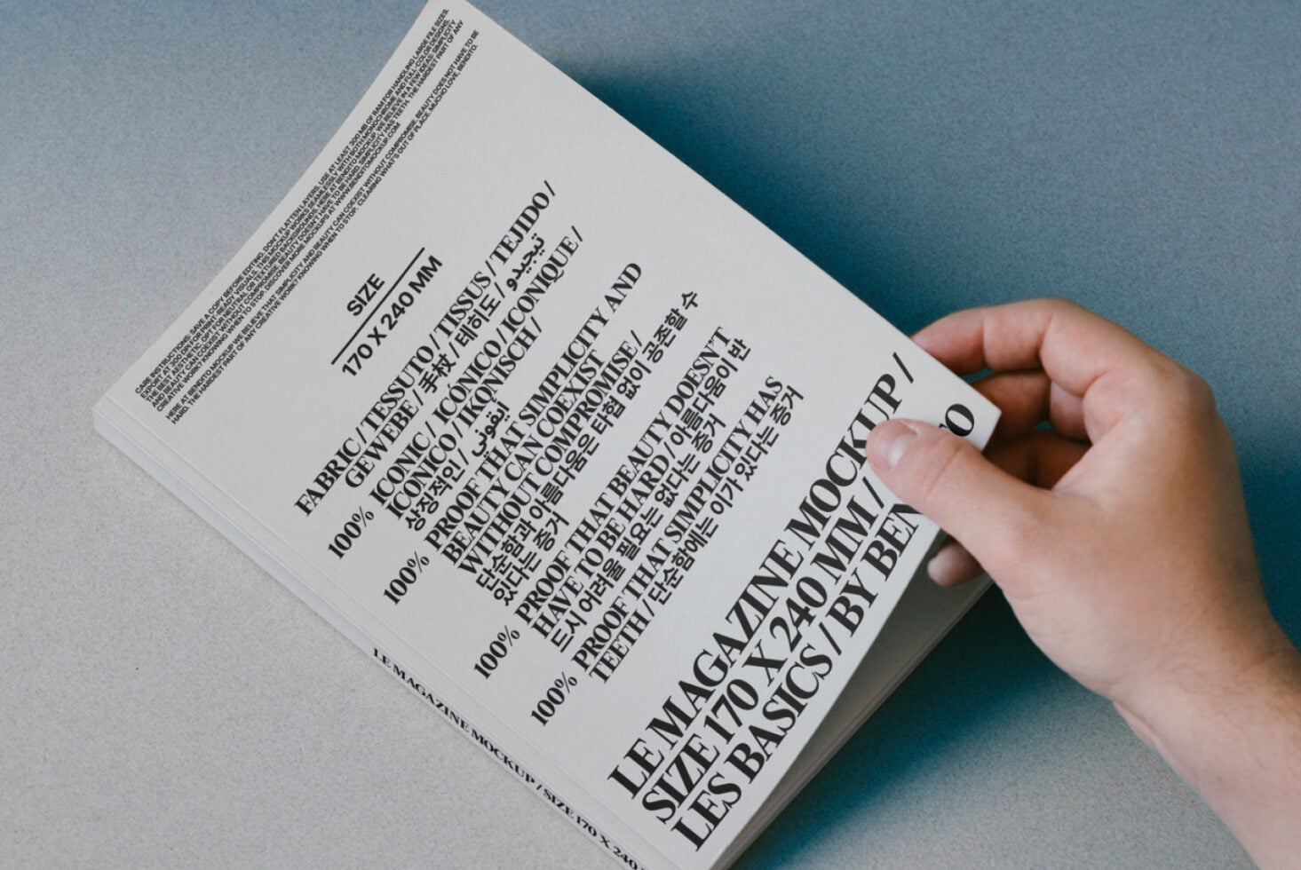 Hand holding white book with multilingual text on blue paper background, back cover