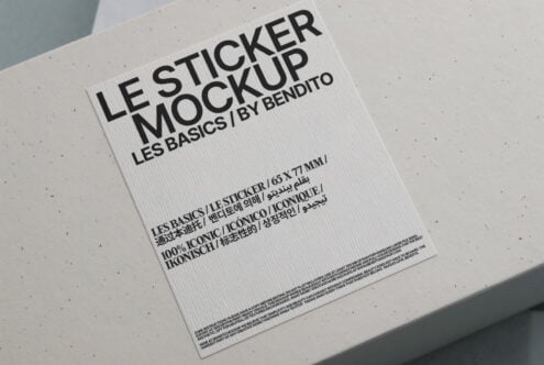 White sticker mockup on beige surface with black handles visible above