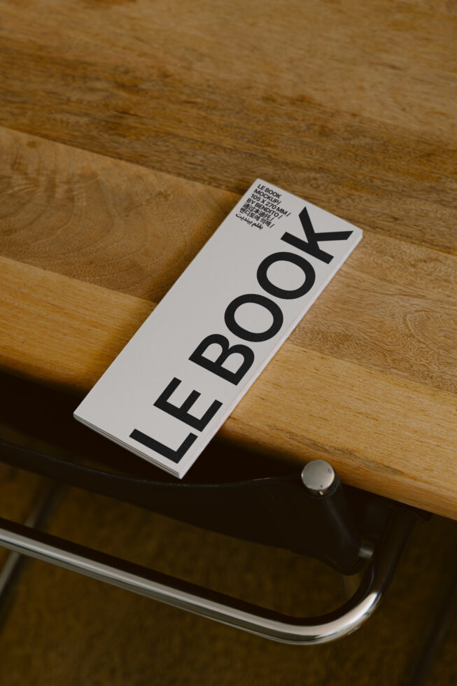 Slim white hardcover book mockup with LE BOOK text on wooden surface