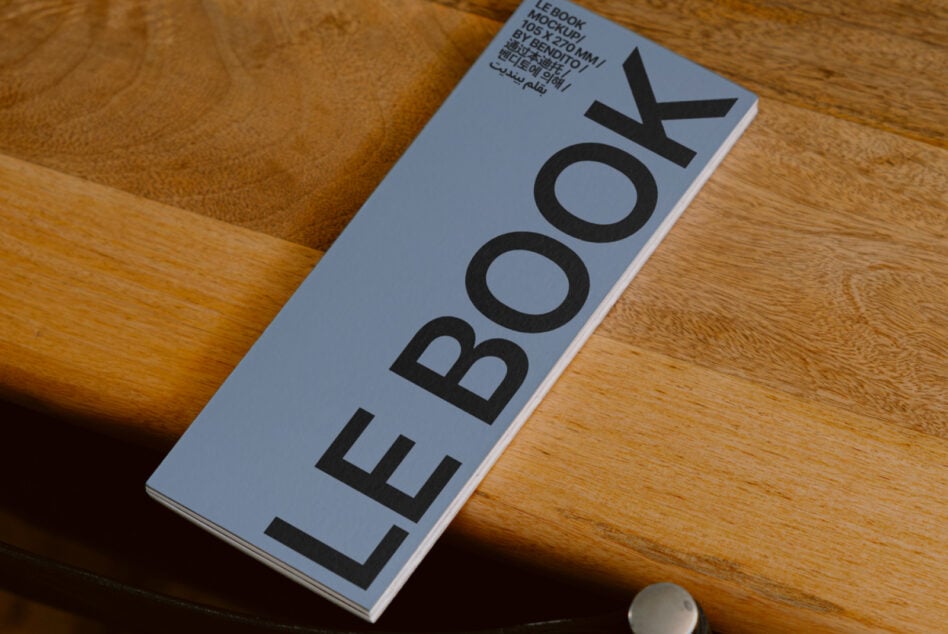 Light blue hardcover book mockup showing LE BOOK spine on wood desk
