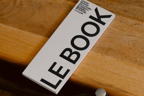 White hardcover book mockup displaying LE BOOK title on wooden table