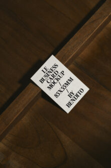 White business card mockup on diagonal wood grain, serif typography, 85x55mm