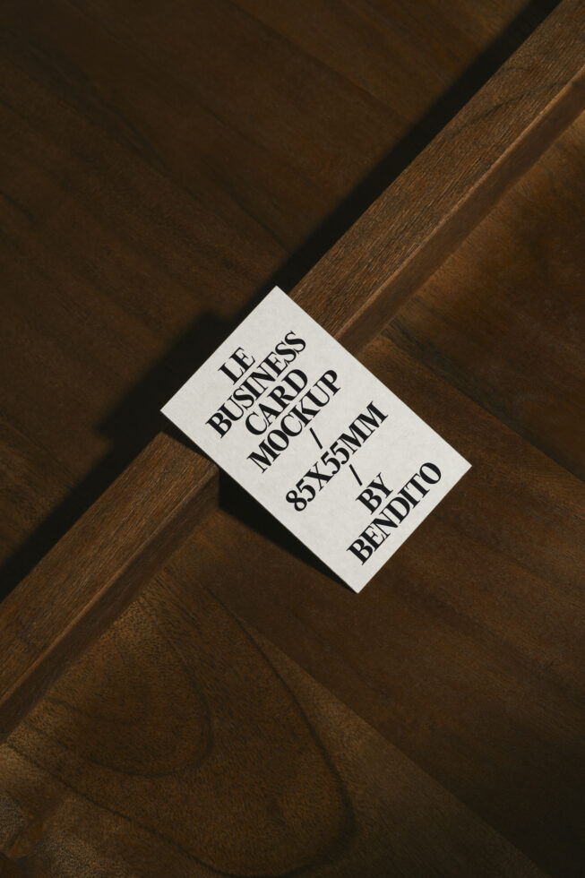 White business card mockup on diagonal wood grain, serif typography, 85x55mm