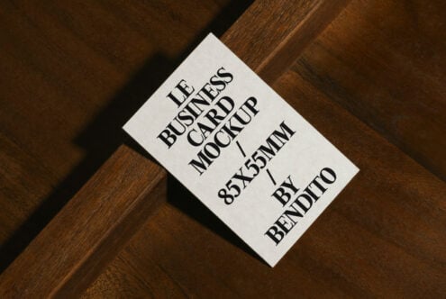 White business card mockup on diagonal wood grain, serif typography, 85x55mm