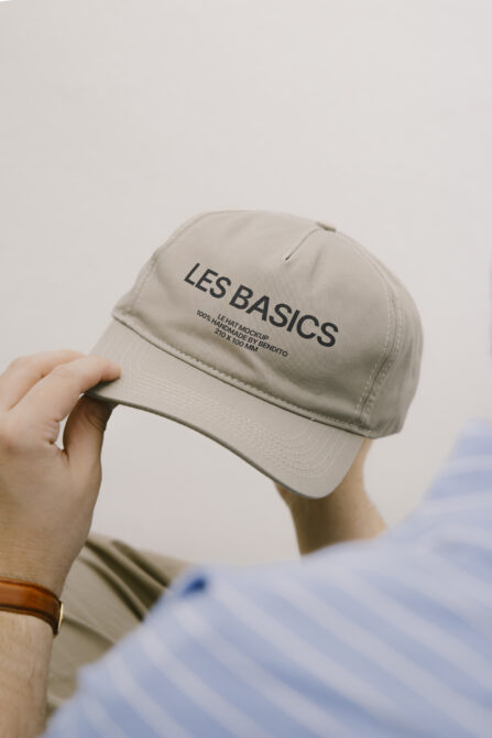 Cream baseball cap held in hand with Les Basics text printed on front