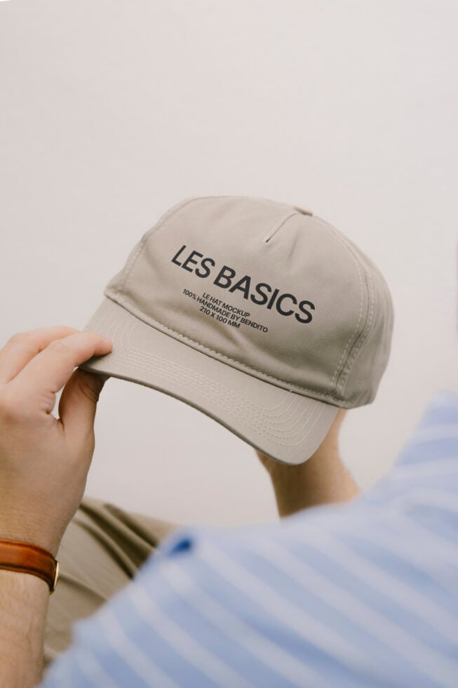 Cream baseball cap held in hand with Les Basics text printed on front