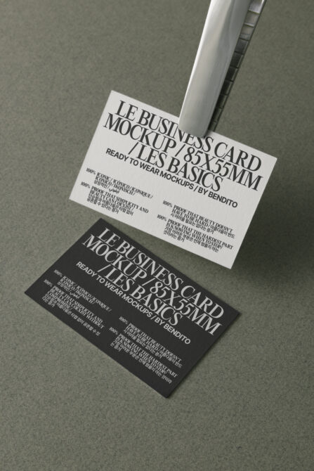 White black business cards overlapped, angled overhead, metallic clip holder shadow