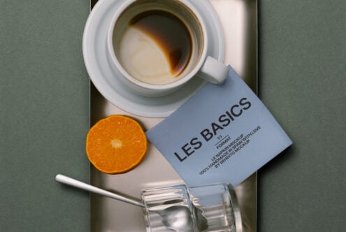 Top down coffee setup with white cup, orange, card, glass vessel on surface