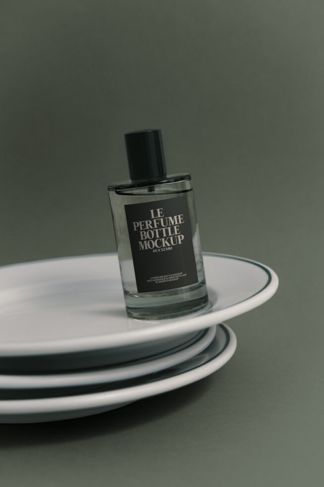 Glass perfume bottle with black label sitting on stacked white plates