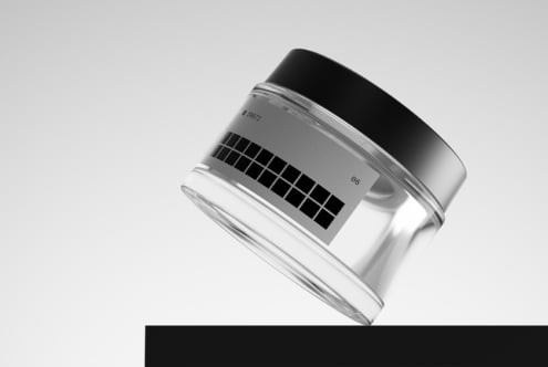 Clear cosmetic jar with silver lid displaying product label on neutral background