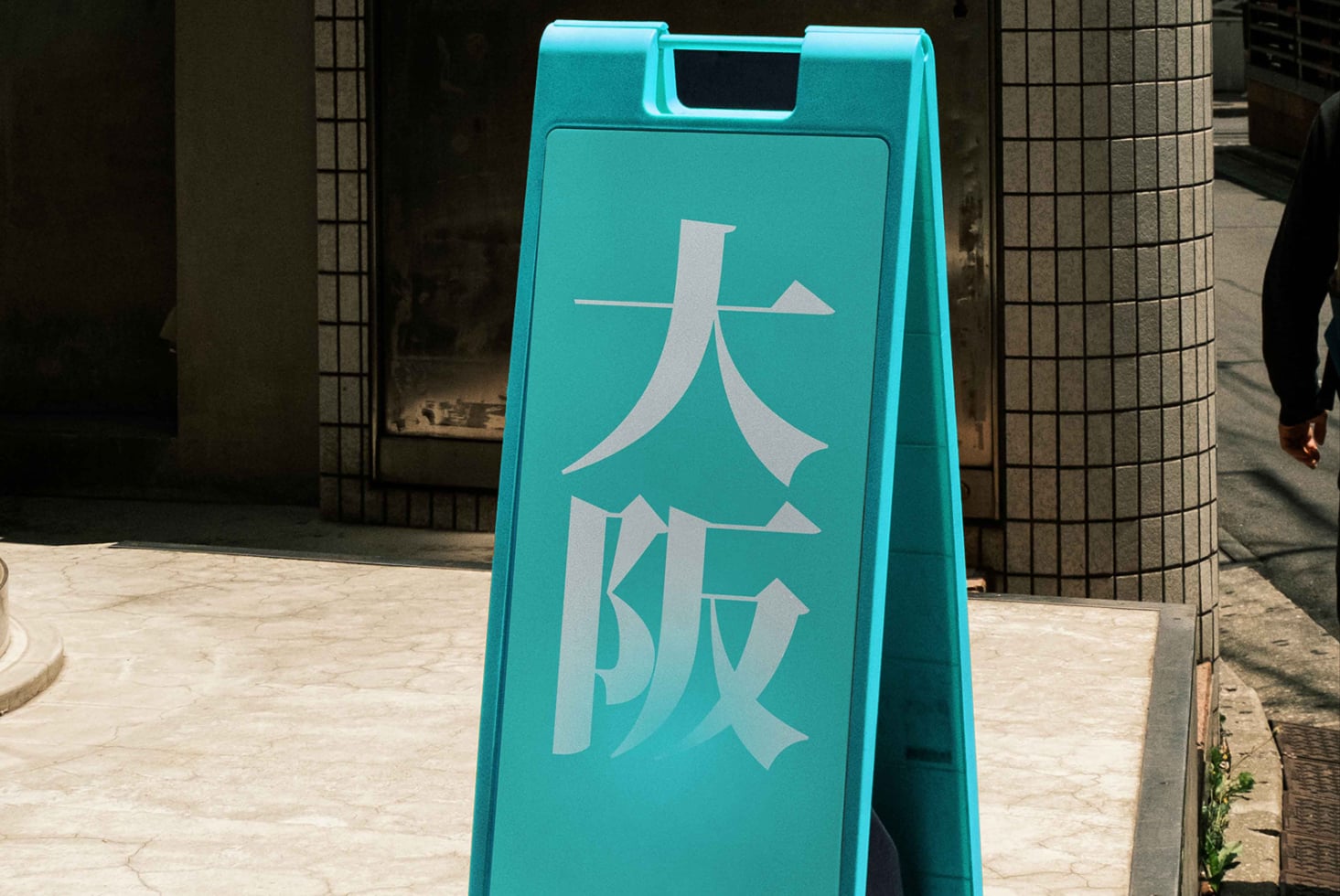 Bright turquoise a-frame sidewalk sign with white Japanese characters outdoors