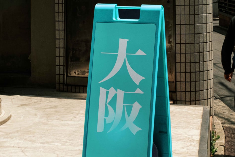 Bright turquoise a-frame sidewalk sign with white Japanese characters outdoors
