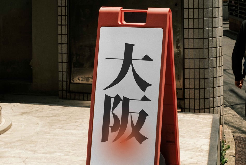 Coral red sandwich board with white panel displaying black Japanese kanji in street