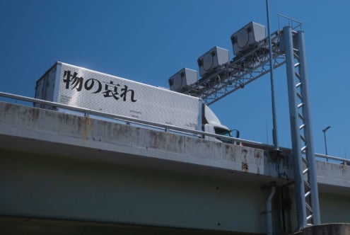 White highway billboard with black Japanese text, metal support structure, clear sky