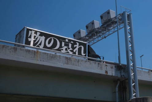 Dark highway billboard with white Japanese text, metal support structure, clear sky