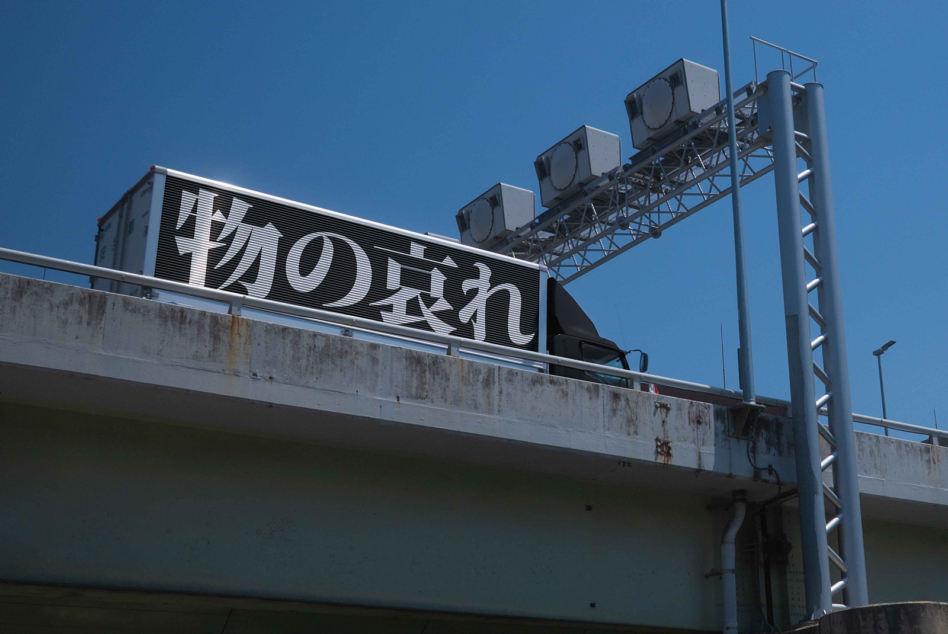 Dark highway billboard with white Japanese text, metal support structure, clear sky