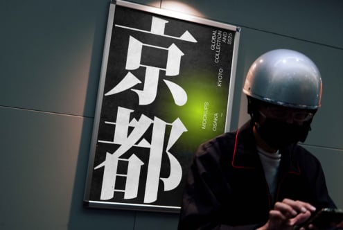 Person in helmet examining framed poster featuring large kanji typography, lime green gradient