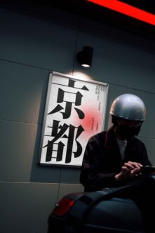 Woman in helmet viewing wall-mounted poster with bold Japanese characters, red gradient background