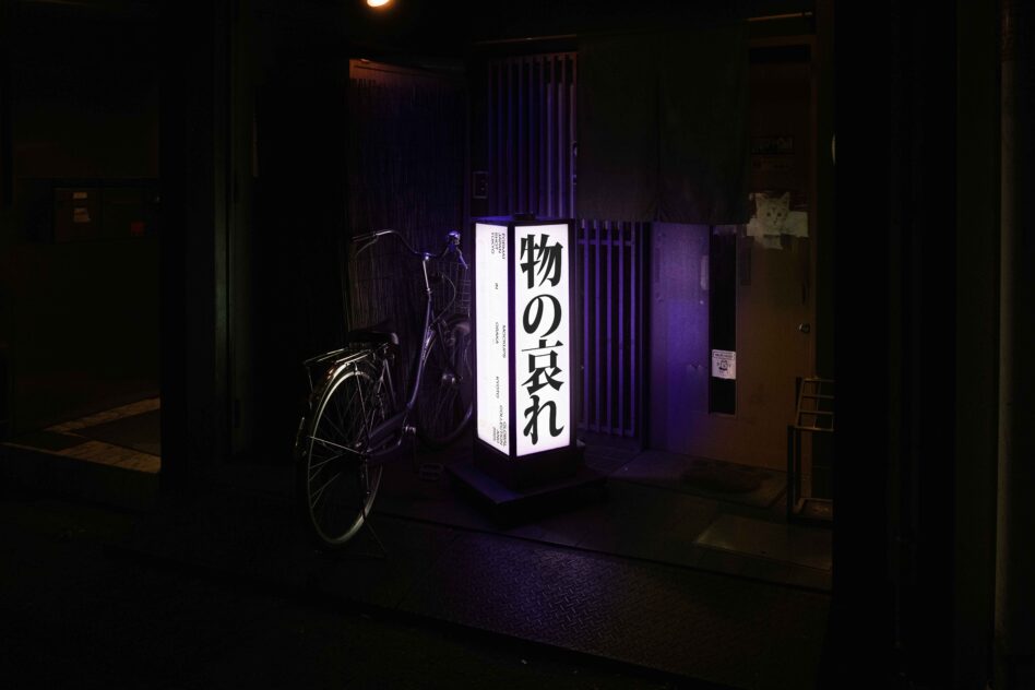 Illuminated cube sign with white Japanese text glowing in dark alley with bicycle nearby