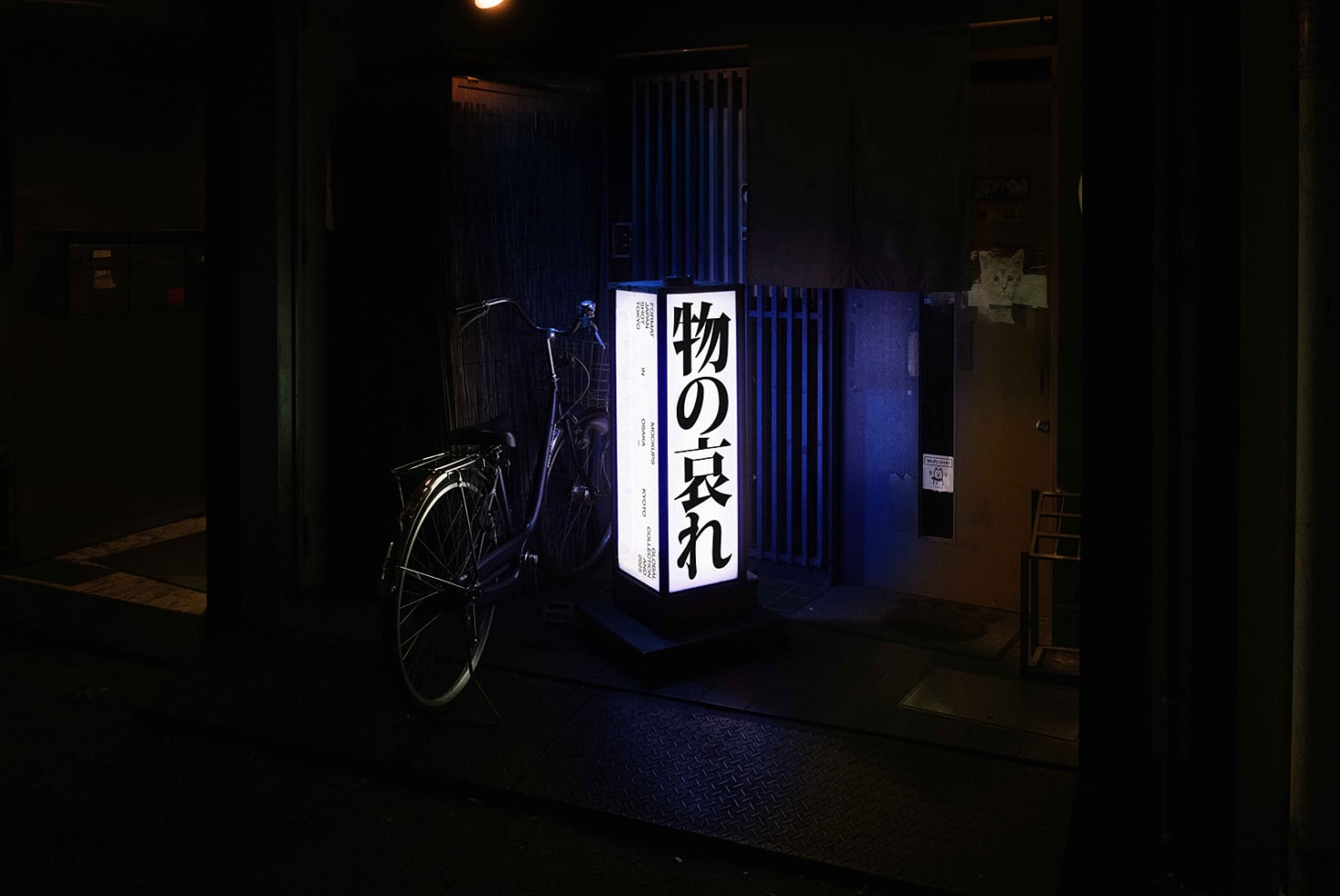 Blue backlit box sign with Japanese typography positioned in dark urban corridor with bike