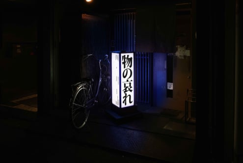 Blue backlit box sign with Japanese typography positioned in dark urban corridor with bike