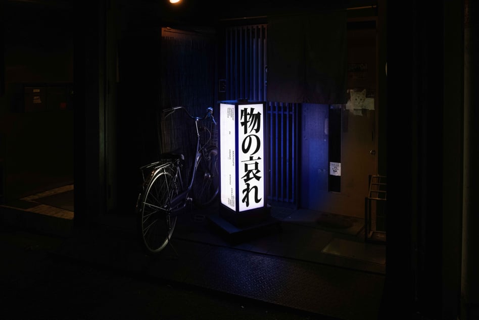 Blue backlit box sign with Japanese typography positioned in dark urban corridor with bike