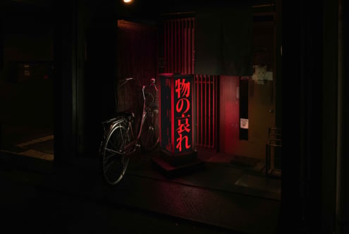Red neon lit cube sign displaying Japanese characters in moody underground passage setting