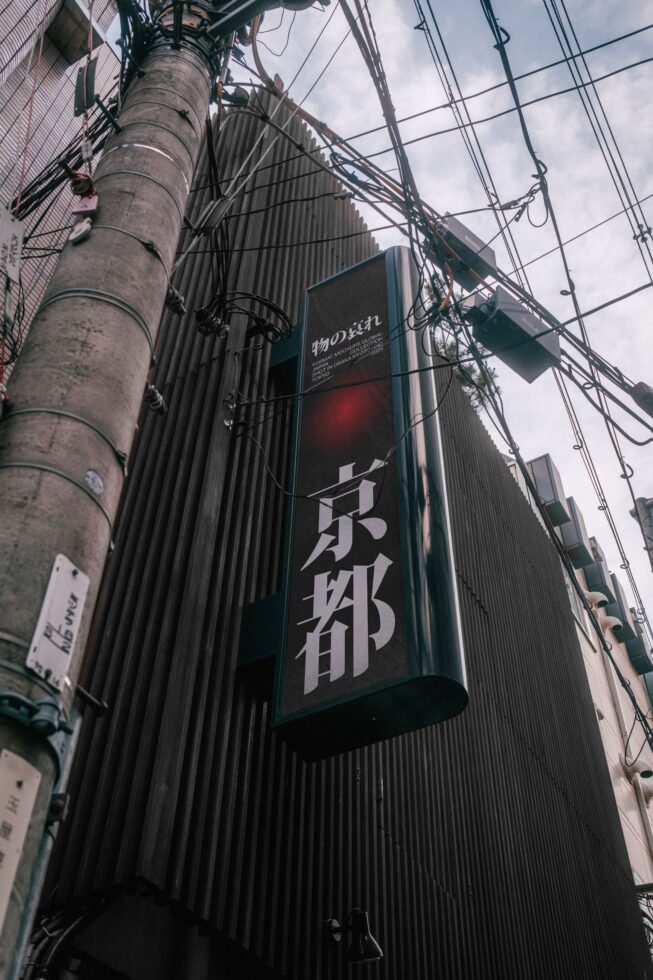 Upward angle of concrete pole, tangled wires, Japanese storefront sign with red glow