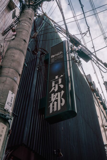 Upward angle of concrete pole, tangled wires, Japanese storefront sign with blue glow