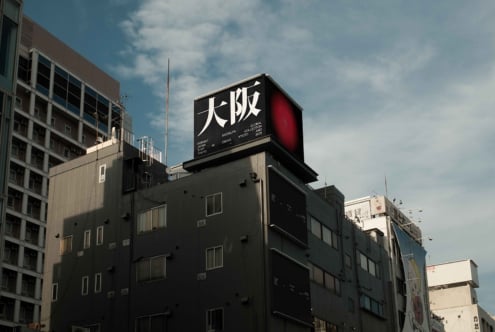 Urban rooftop billboard with red accent, large white Japanese characters visible