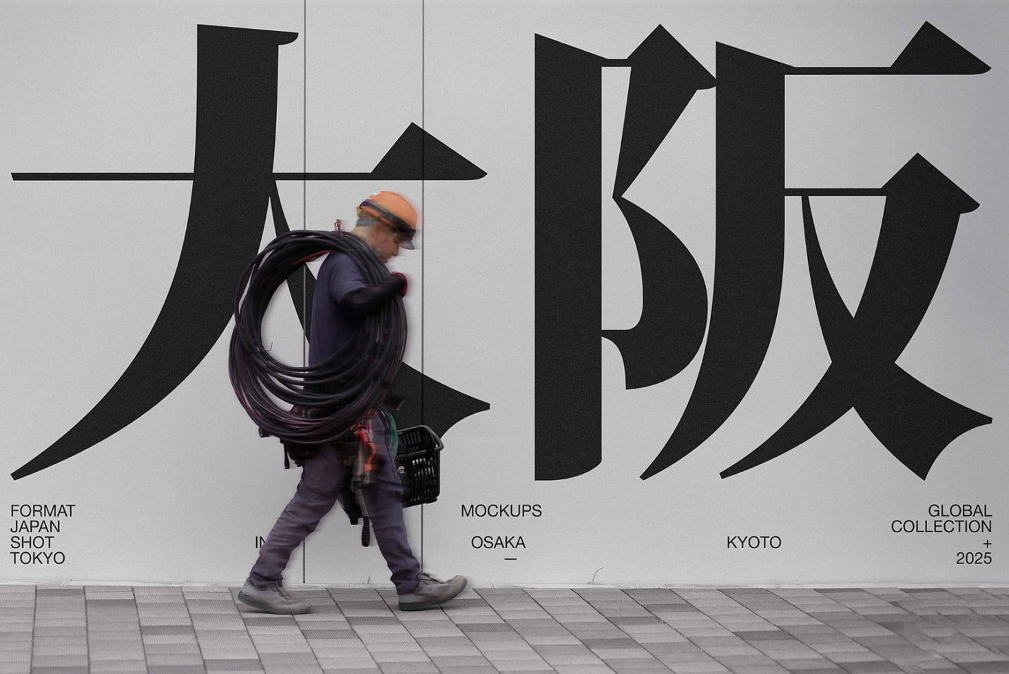 Worker carrying cable walking past bold Japanese characters on light wall