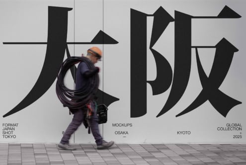 Worker carrying cable walking past bold Japanese characters on light wall