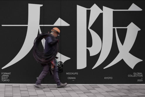 Worker carrying cable walking past large Japanese characters on dark wall