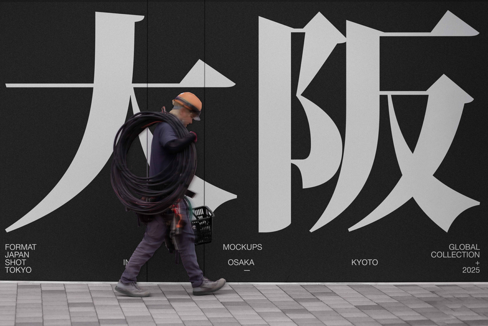 Worker carrying cable walking past large Japanese characters on dark wall