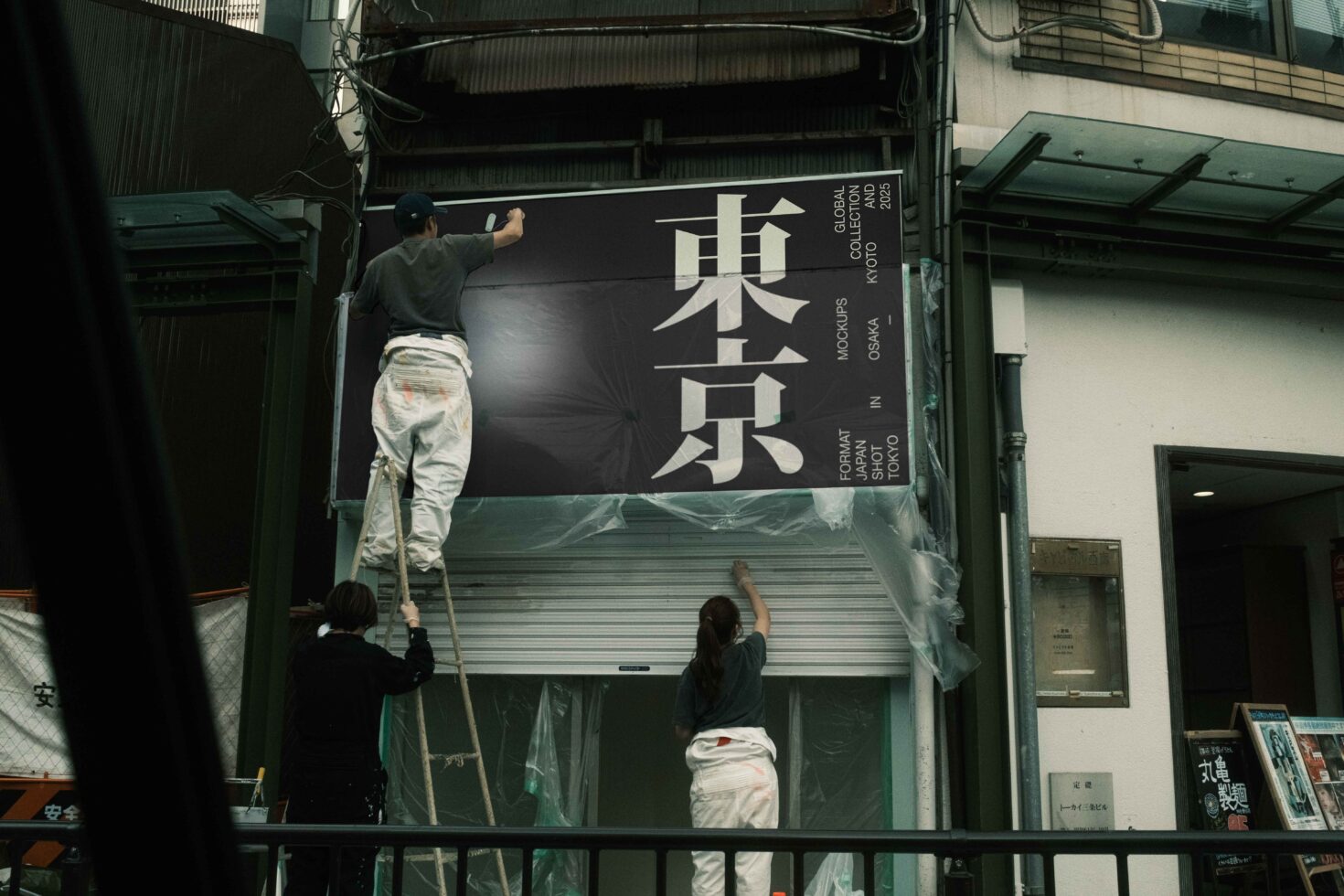 Workers on ladder installing storefront sign with large Japanese characters on black background