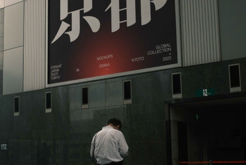 Large building banner with bold Japanese characters, person standing below against green facade