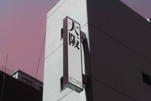 Tall black vertical sign with white kanji mounted on building under pink sky