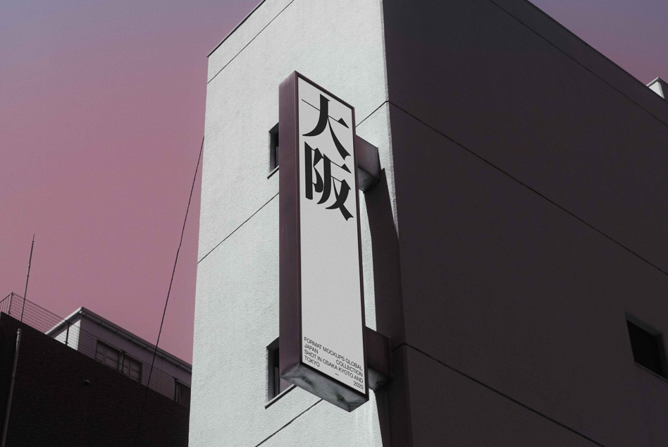 Tall black vertical sign with white kanji mounted on building under pink sky